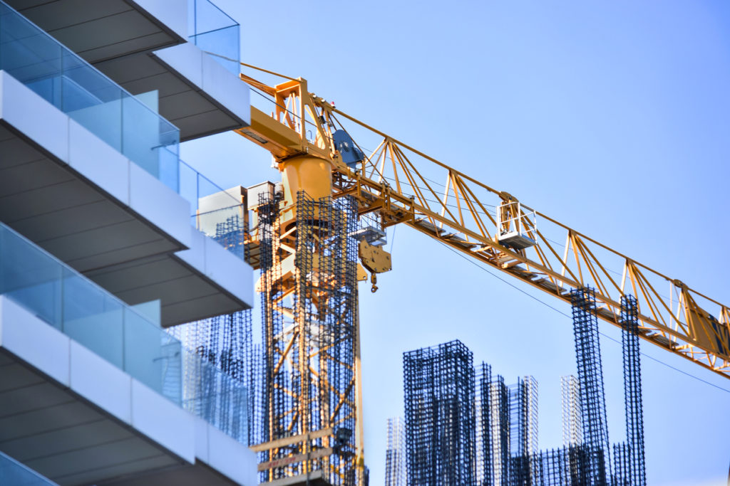Yellow construction crane and under construction high-rise building with glass facade from low angle against blue sky